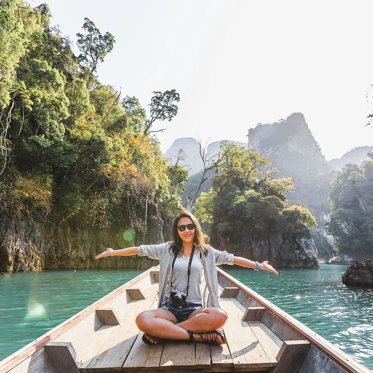 Woman tourist sitting on boat in tropical location with arms out, smiling.
