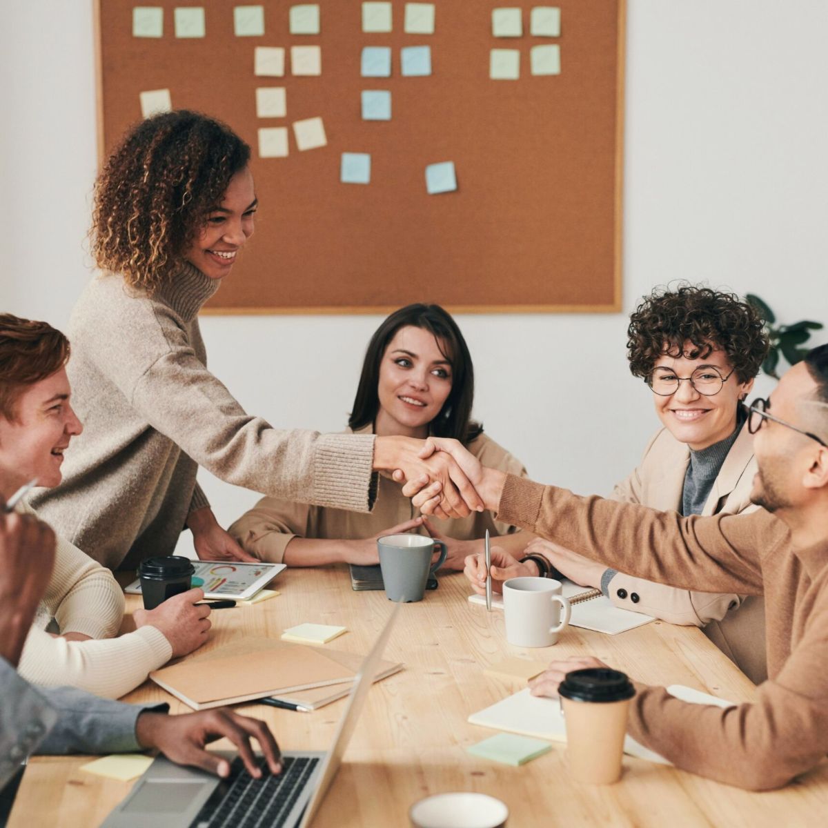 professionals sitting at table, two shaking hands.
