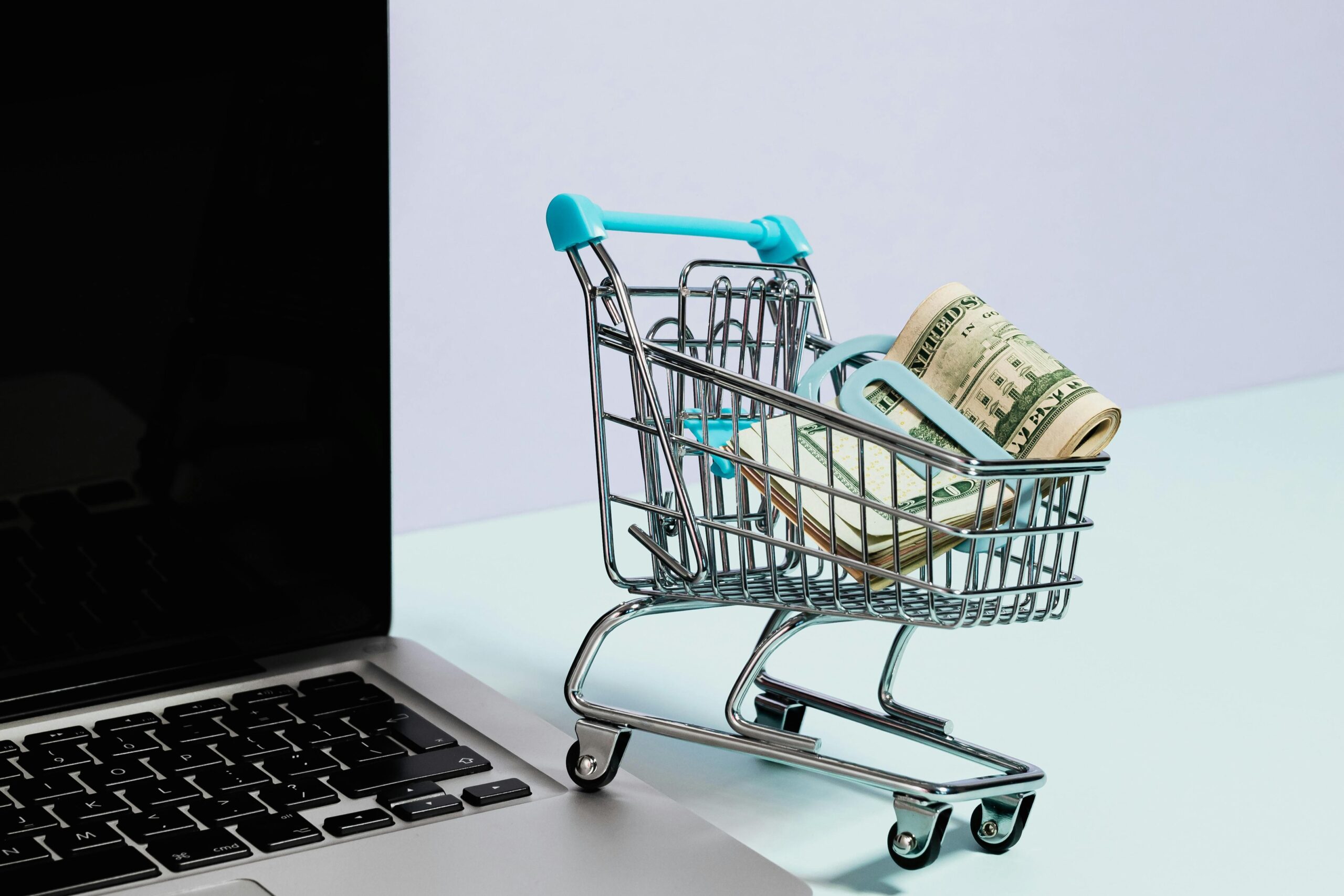 small shopping cart with money inside, resting near a laptop computer
