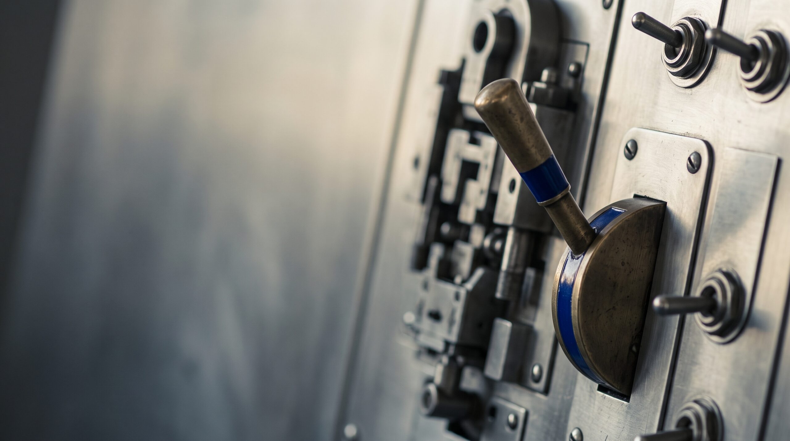 A brass lever with a blue accent is mounted on a brushed steel control panel with blurred dials.