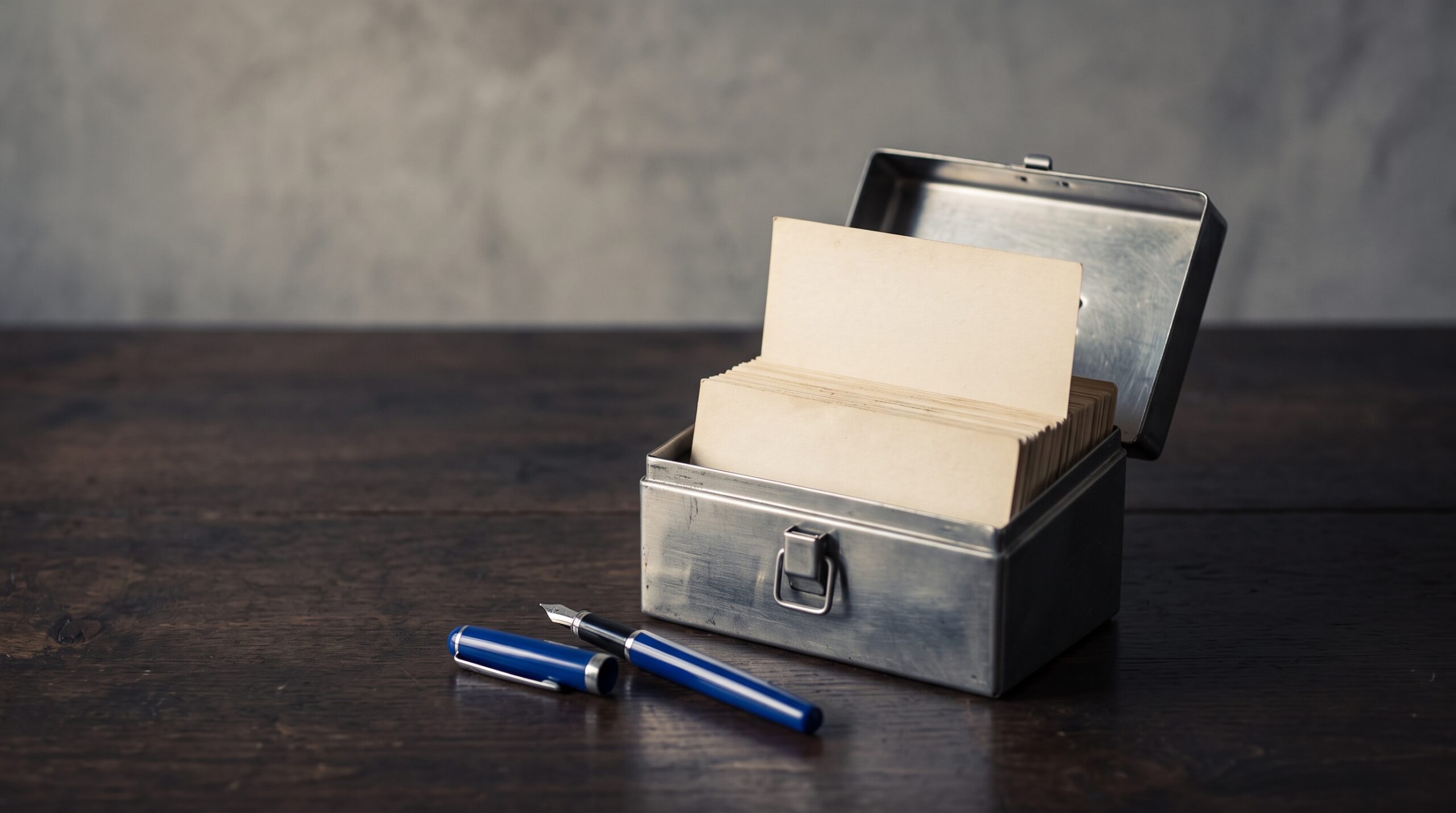 Open steel index-card box with a stack of swipe-file cards and a blue fountain pen